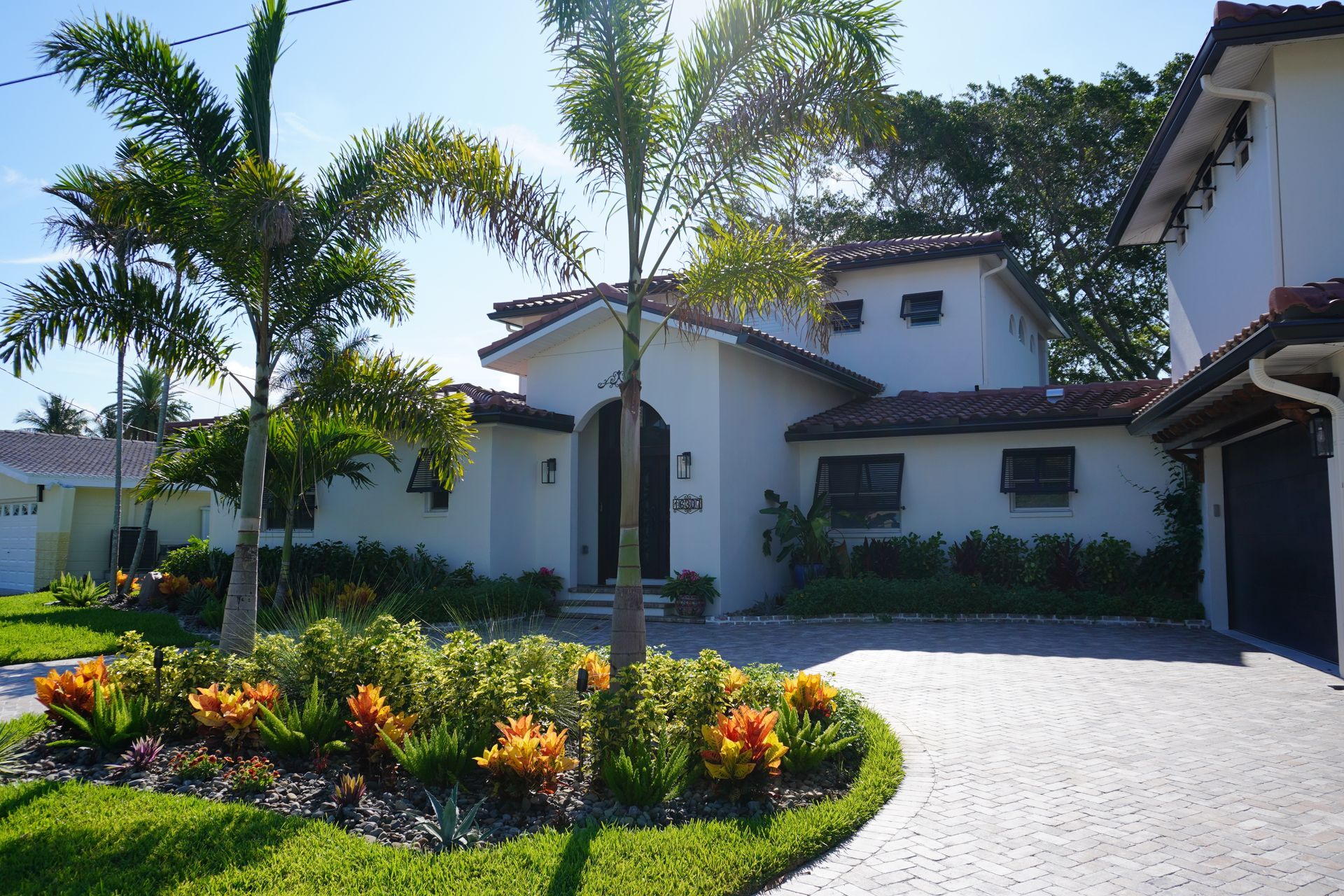 White stucco house with palm trees, landscaped flower bed, and a curved driveway under a blue sky