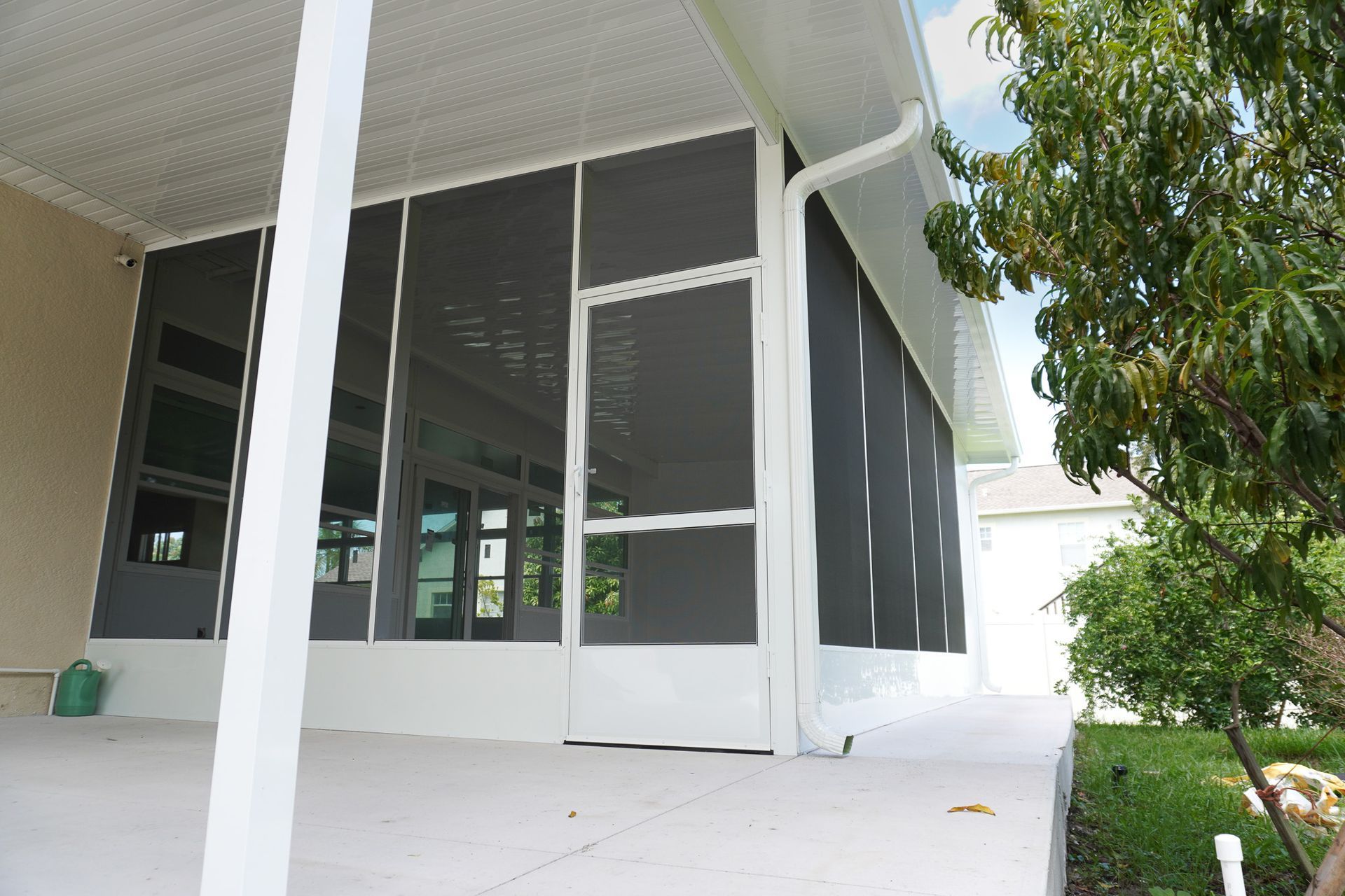 Screened porch with white columns, gray mesh panels, and a concrete patio beside a green lawn.
