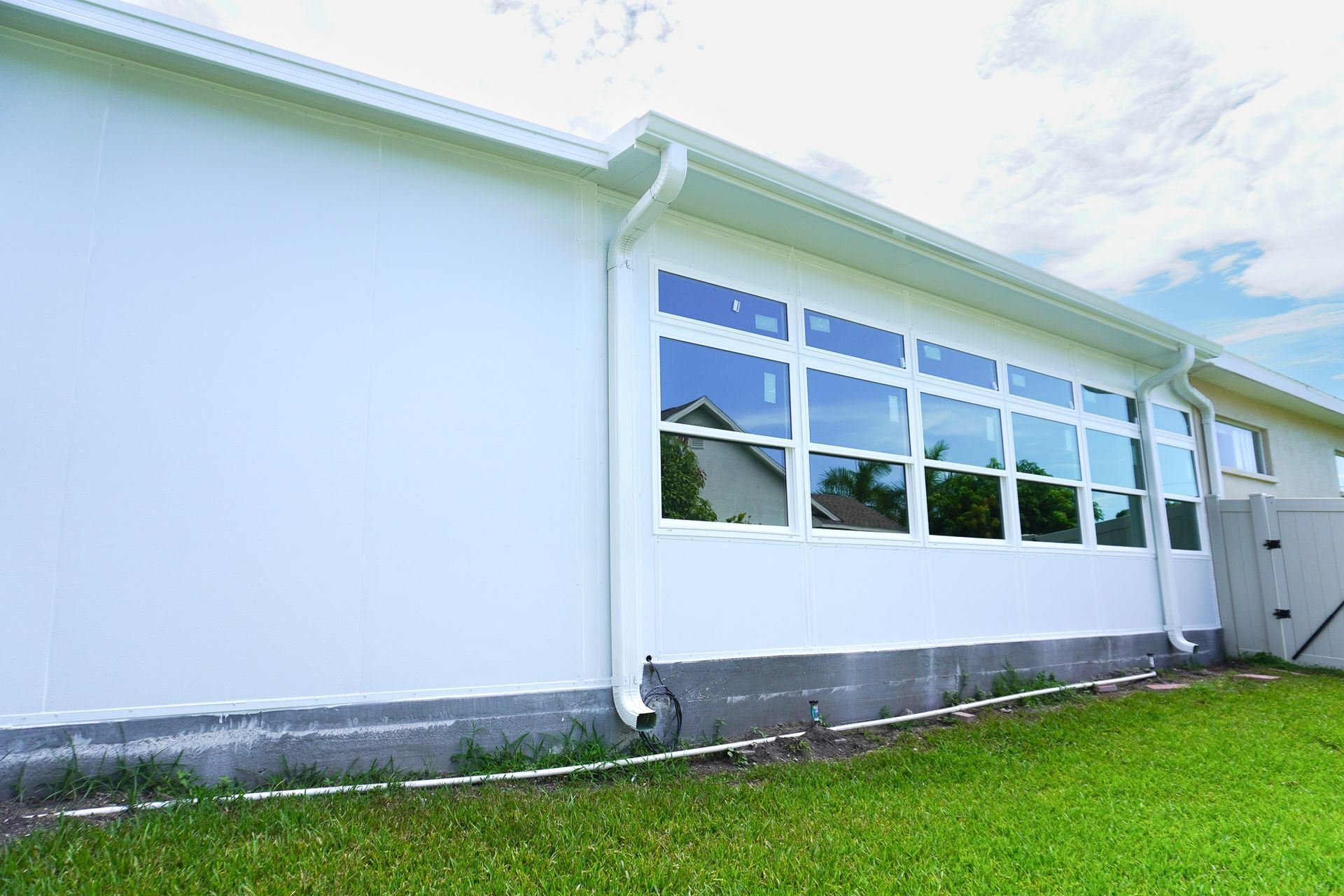 White building exterior with large windows, gray foundation, and green lawn under a bright sky