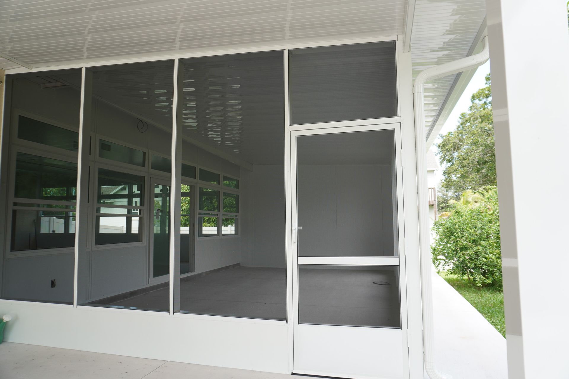 Screened porch with white-framed windows and gray floor, overlooking greenery outside