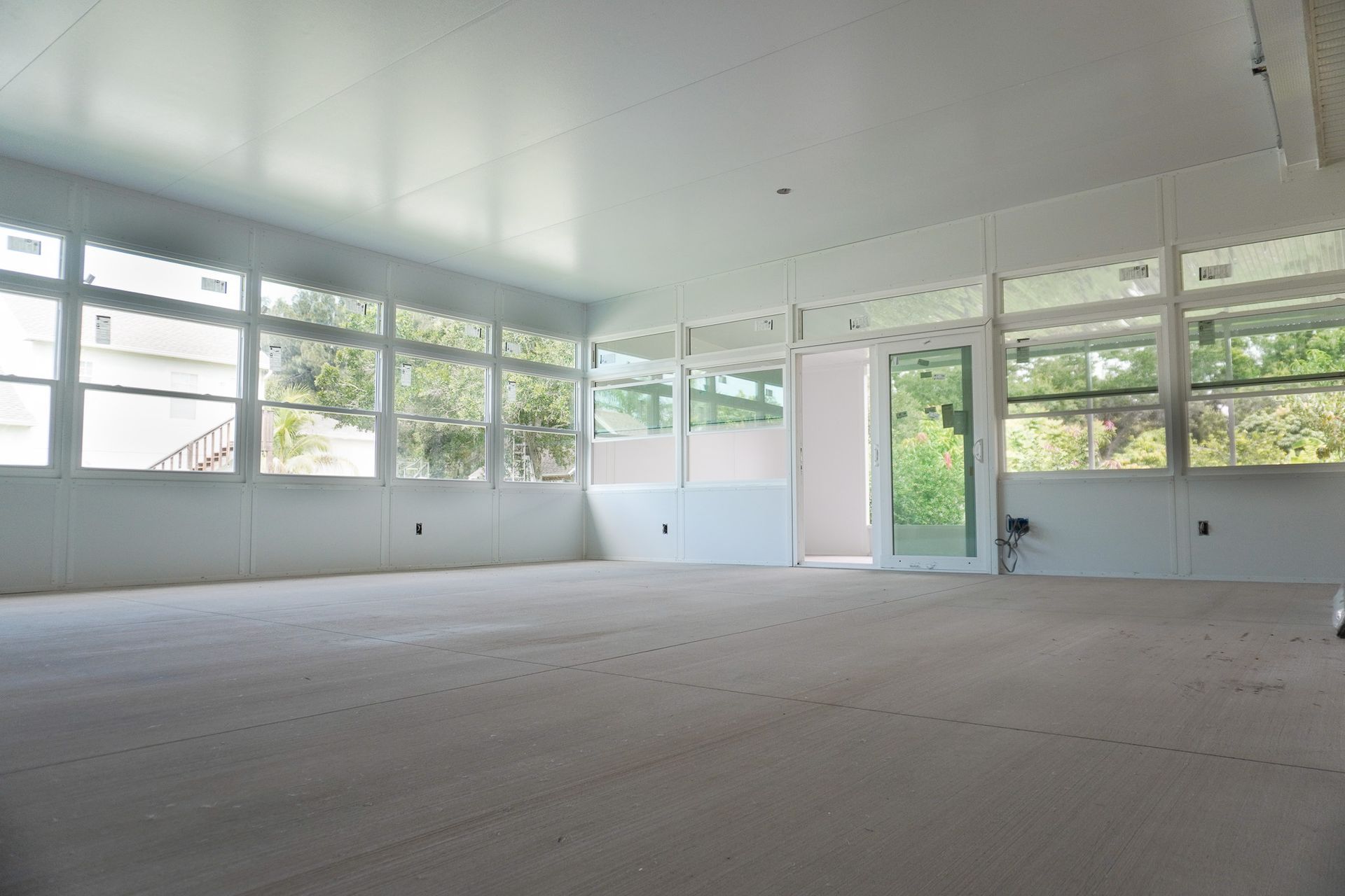 Empty white room with large windows, wood floor, and bright natural light