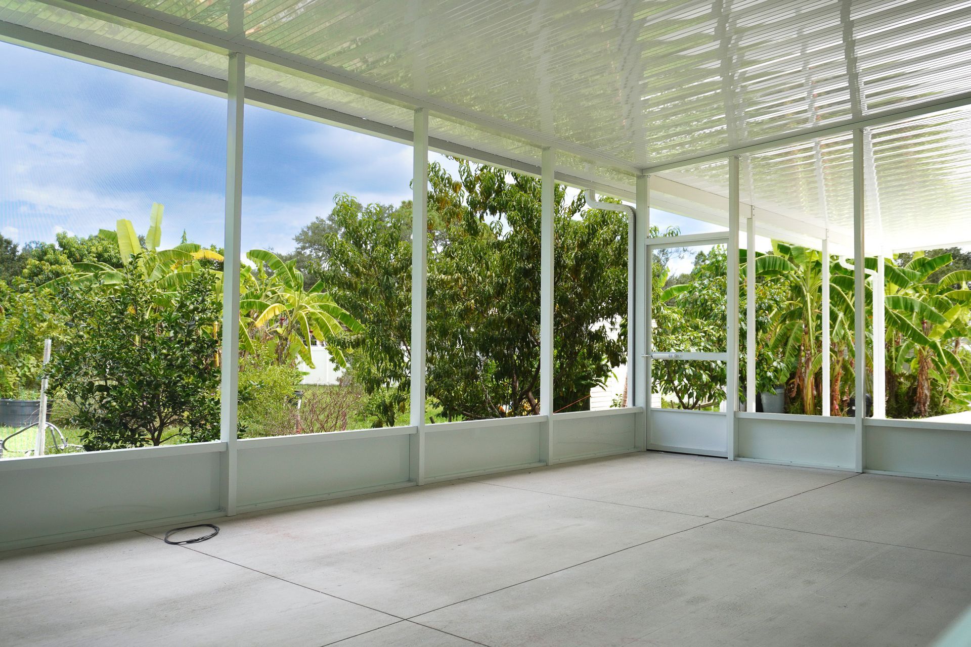 Screened porch with white walls and roof, overlooking lush green trees and blue sky.