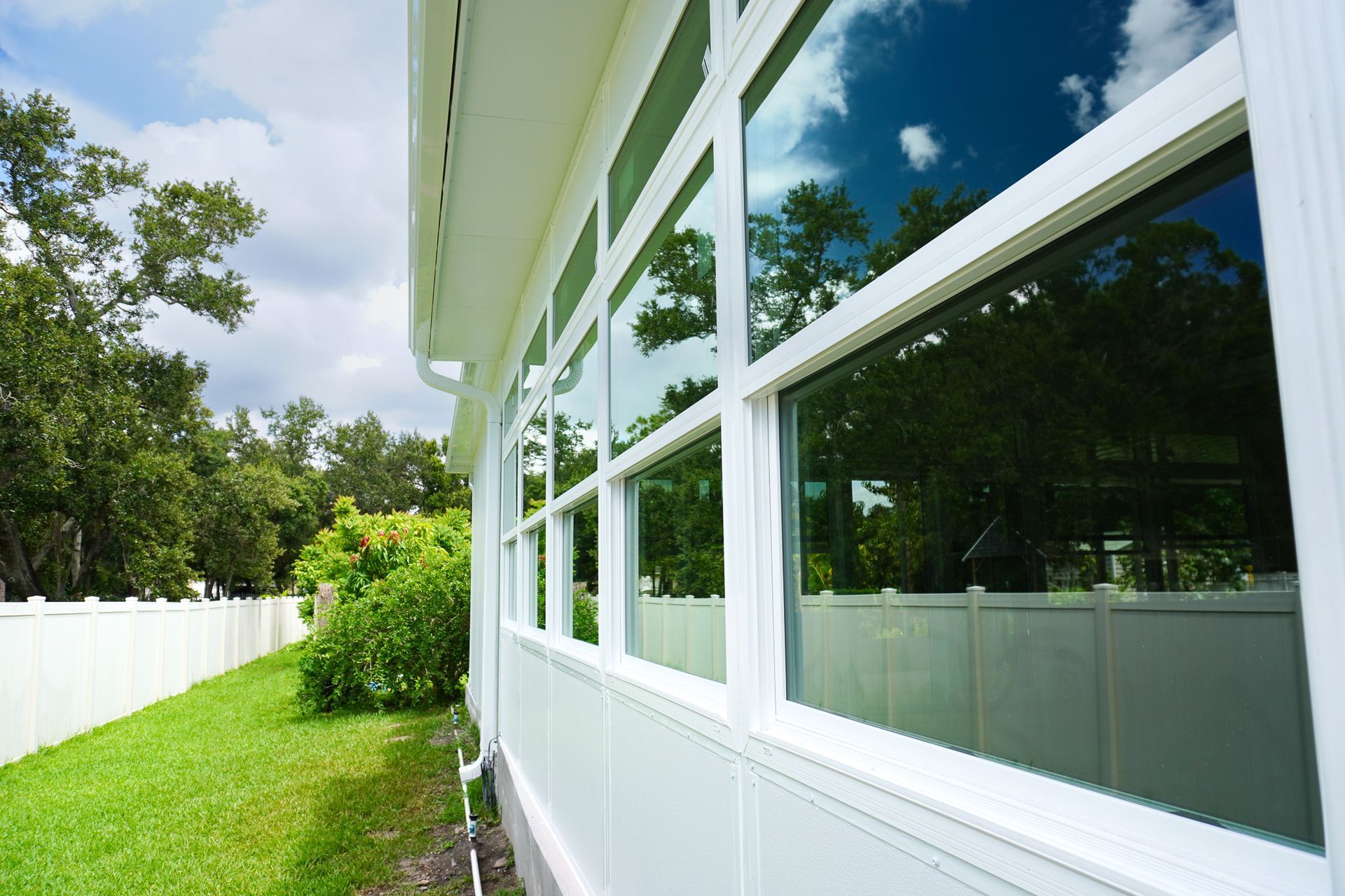 White house exterior with large windows, green lawn, and trees reflecting in the glass