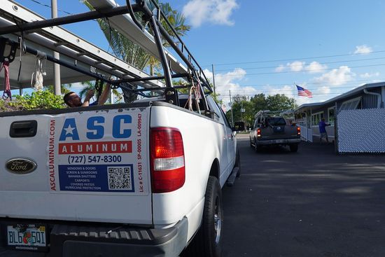 White utility truck with ASC sign parked in a lot under a blue sky, with another vehicle ahead.