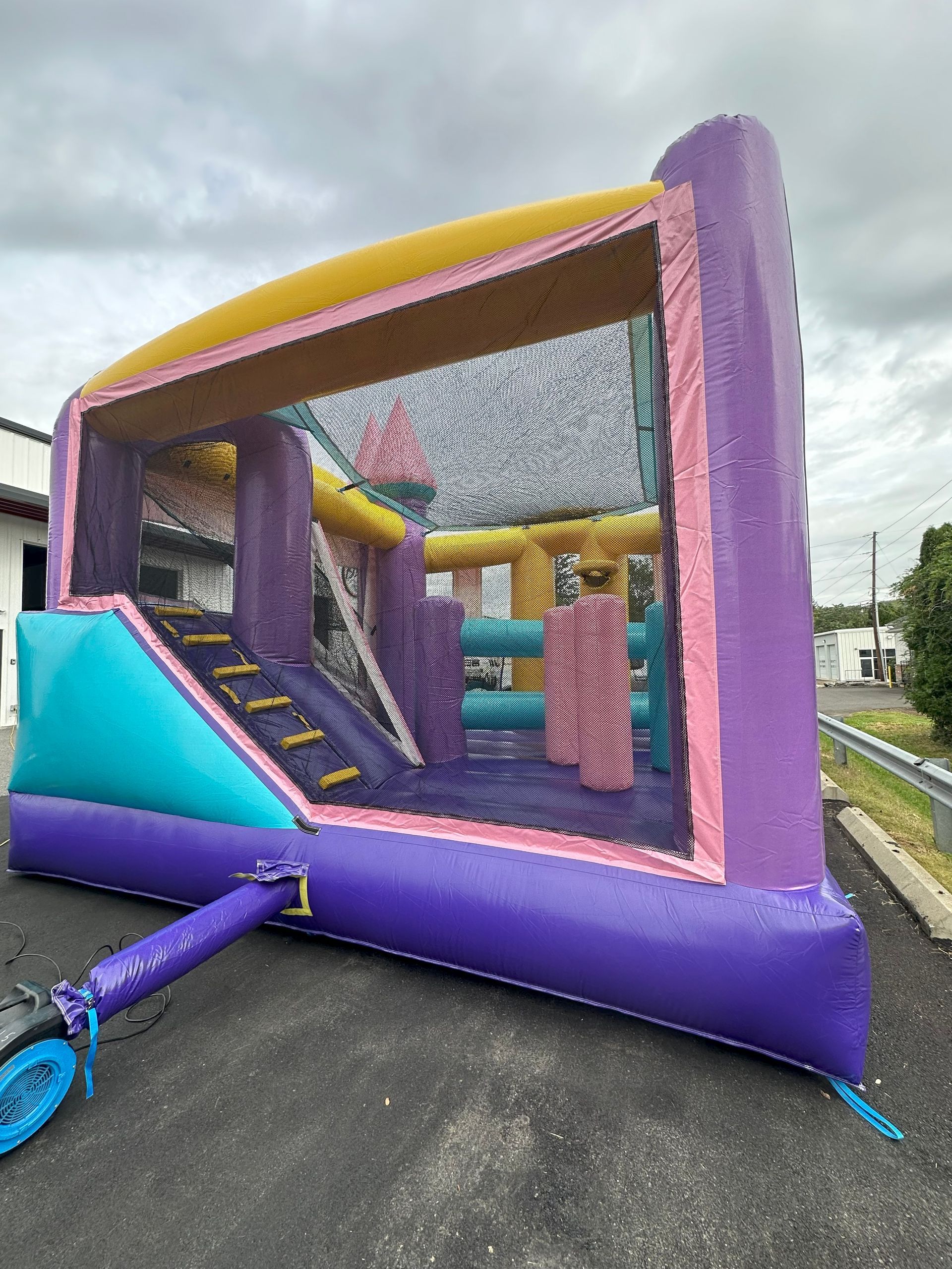 Purple and turquoise inflatable bounce house on asphalt; cloudy sky in background.