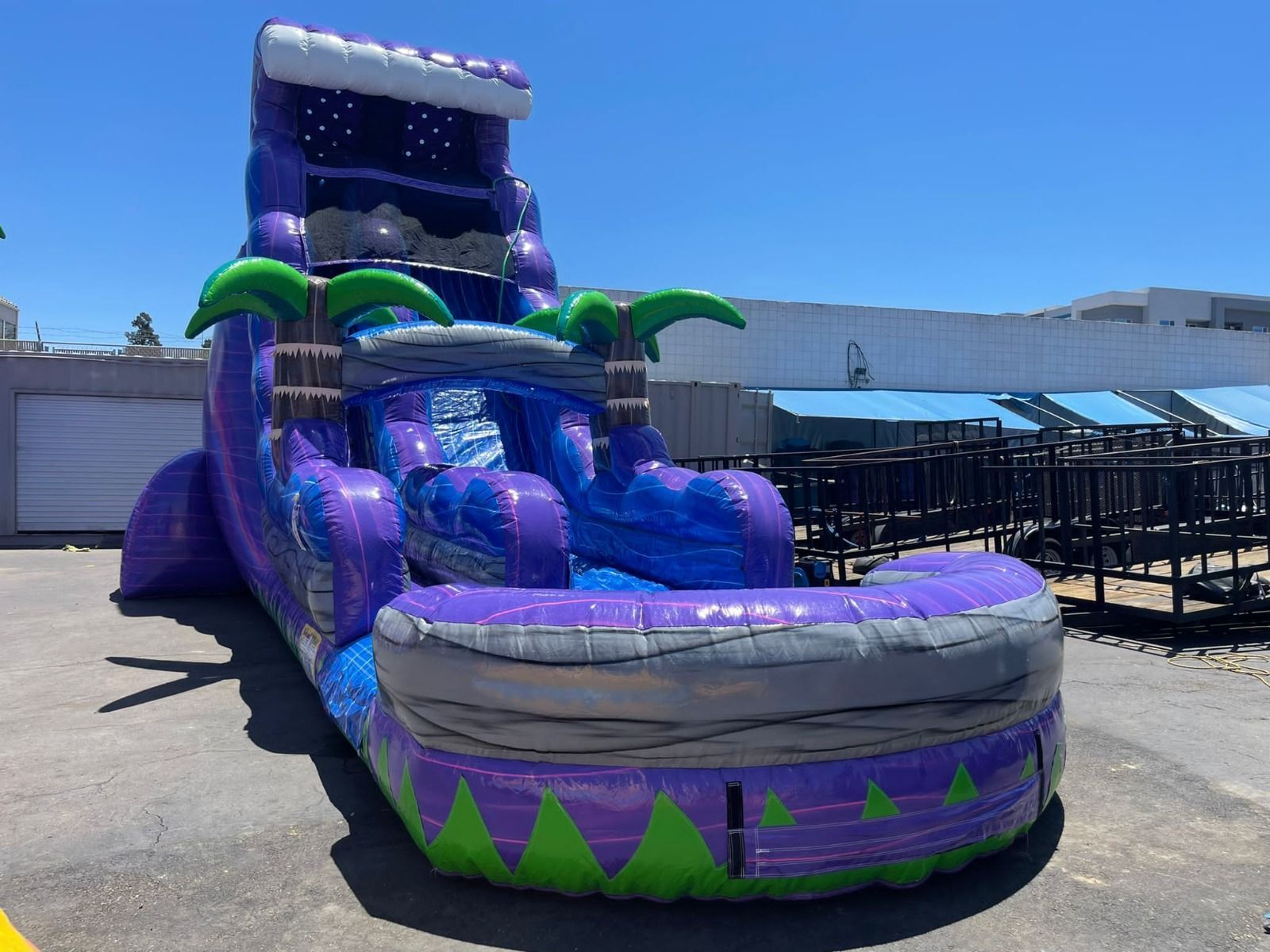 Purple inflatable water slide with green accents in an outdoor parking lot under a clear blue sky