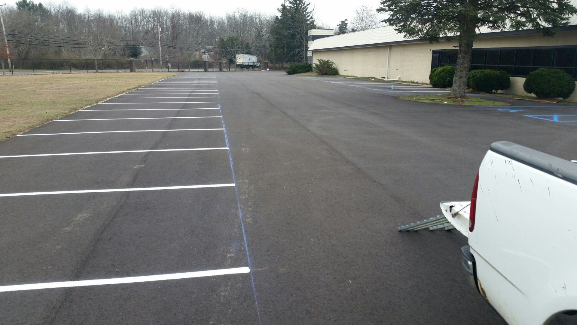 A freshly paved parking lot with white painted stall lines, viewed from the rear of a white pickup truck.