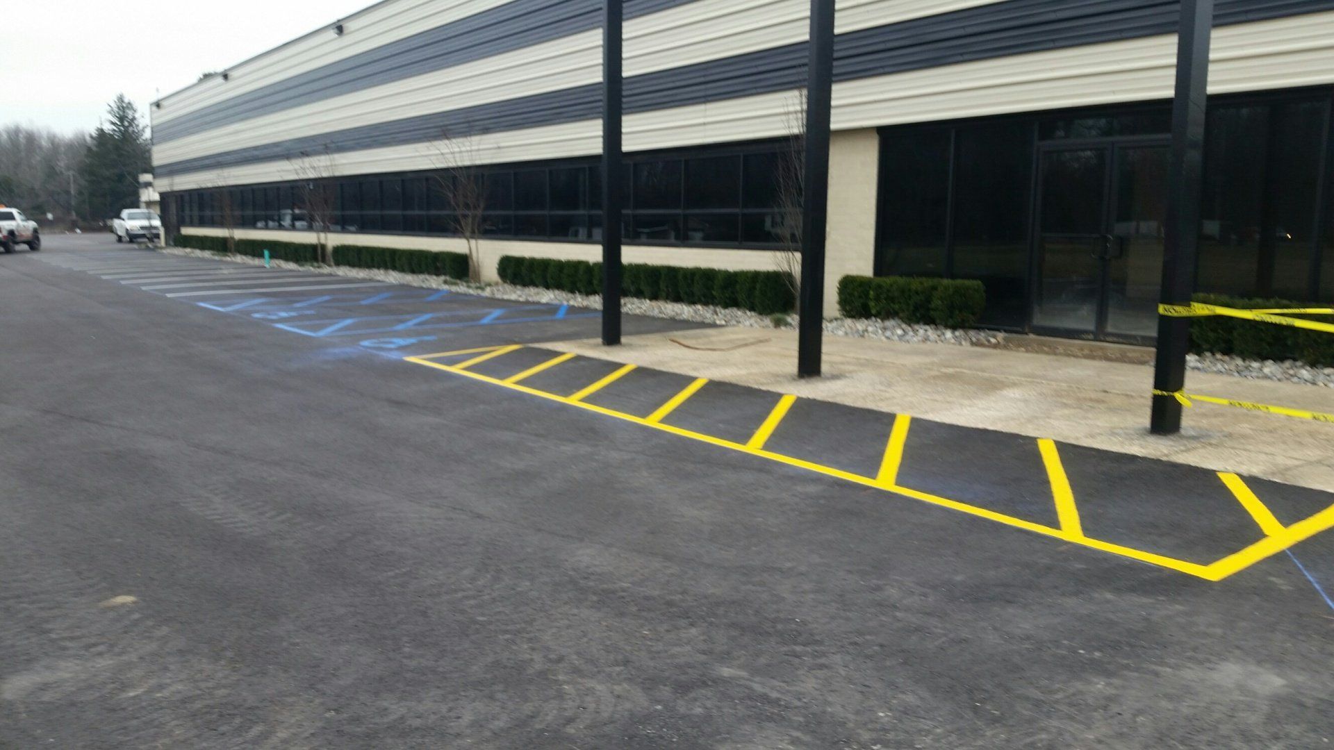 A commercial building exterior with newly painted yellow and blue parking space markings on a fresh asphalt lot.