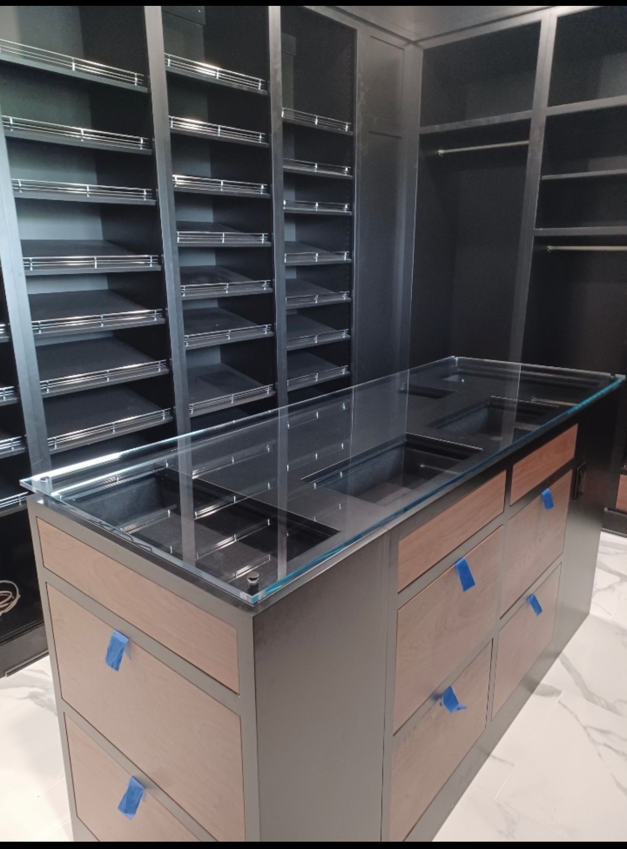 A walk in closet with lots of shelves and drawers and a glass counter top.