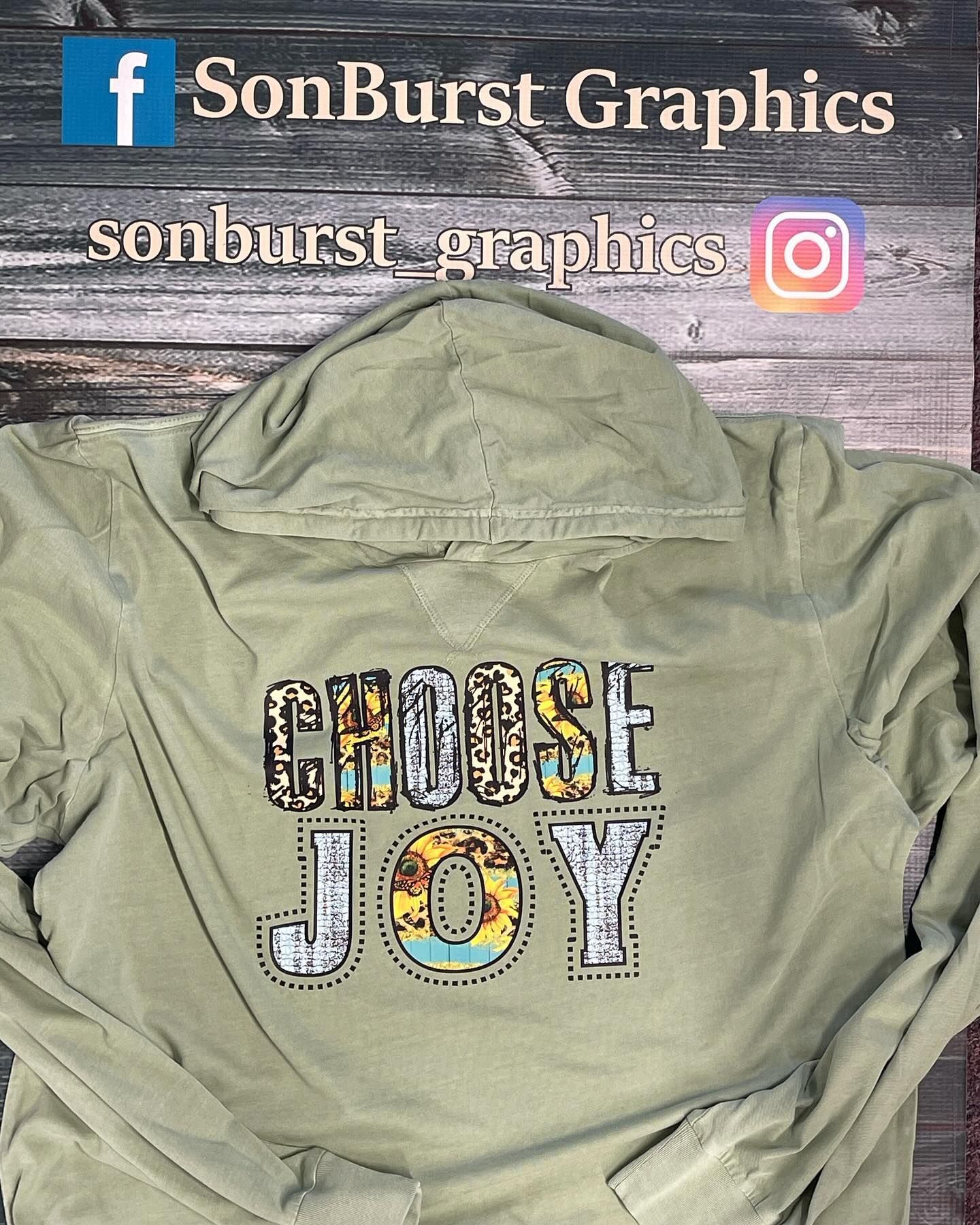 A hoodie that says choose joy is sitting on a wooden table.