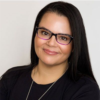 Woman with long dark hair, glasses, and a black top smiling at the camera.