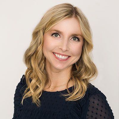 Blond woman with a warm smile in a dark blue top against a white background.