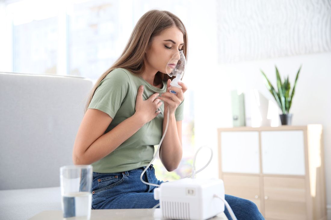 Woman using a nebulizer for breathing treatment in a brightly lit room.