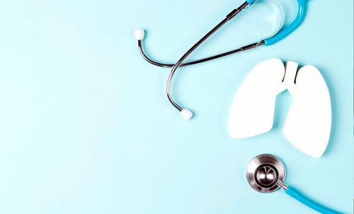 Blue stethoscope next to white lung model on a light blue background, medical concept.