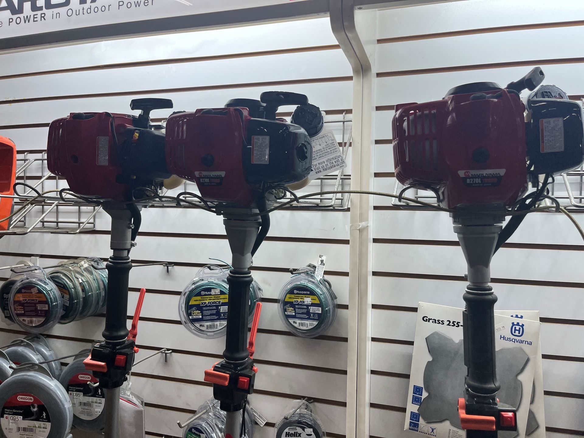 Two red gas-powered auger drills on display in a hardware store.