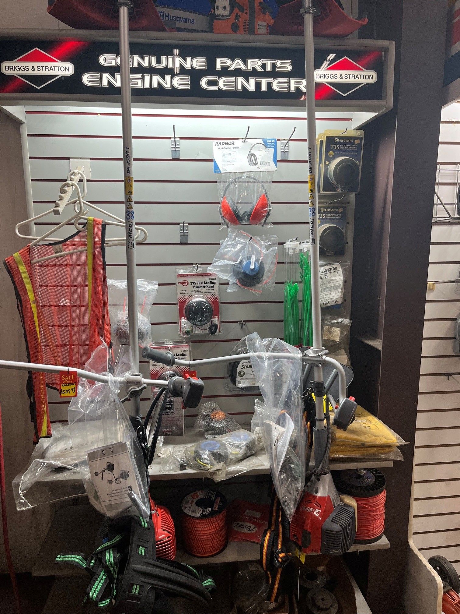 Display wall with engine components, hoses, and tools on shelves under a sign.