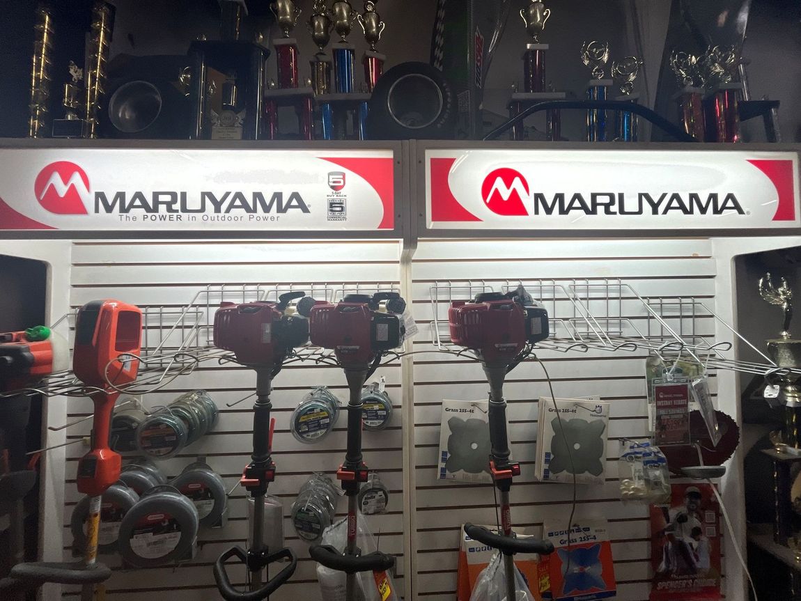Maruyama-branded display wall with red and black lawn and garden power tools on hooks and shelves.