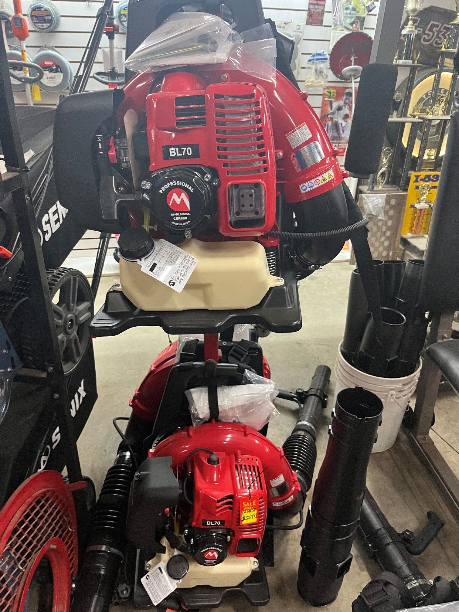 Red backpack leaf blower displayed on a store shelf with accessories and other equipment nearby.