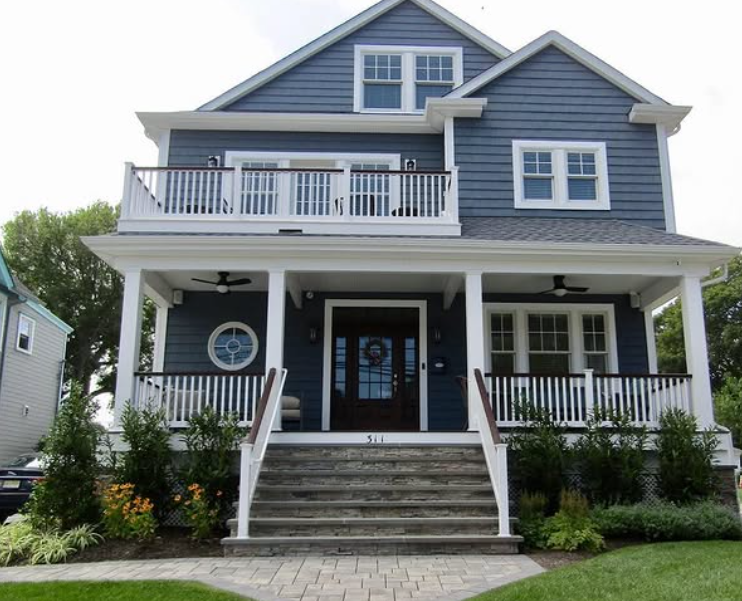 Two-story blue house with white trim, front porch, balcony, and stone steps leading to a dark front door