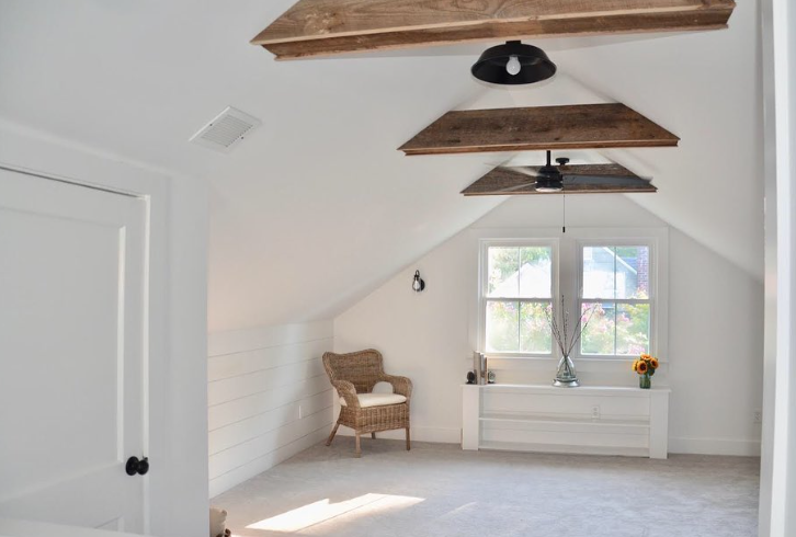 Bright white attic bedroom with wood beams, window, and wicker chair