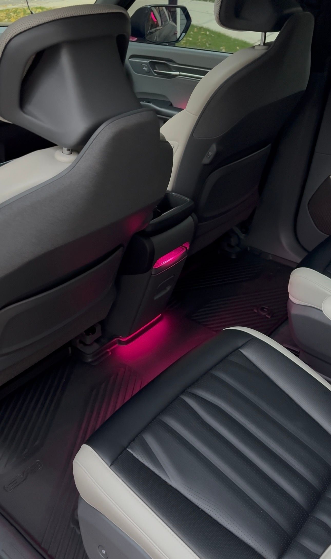 Car interior with black and white seats, pink ambient lighting under seats and console.