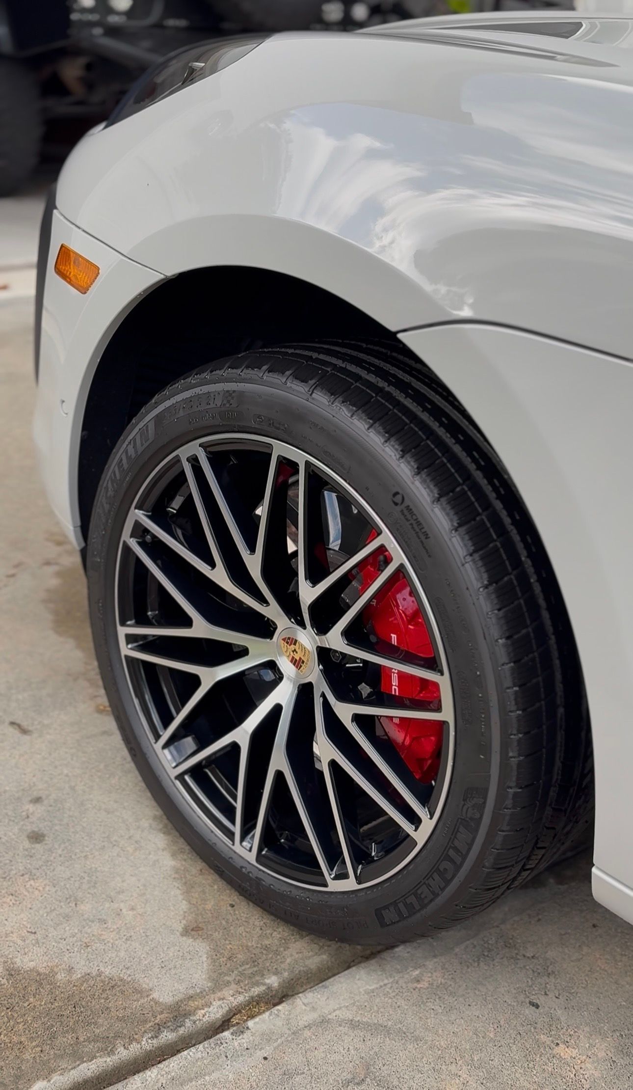 Close-up of a silver car's front tire with black and silver rims, red brake calipers, and a black tire.