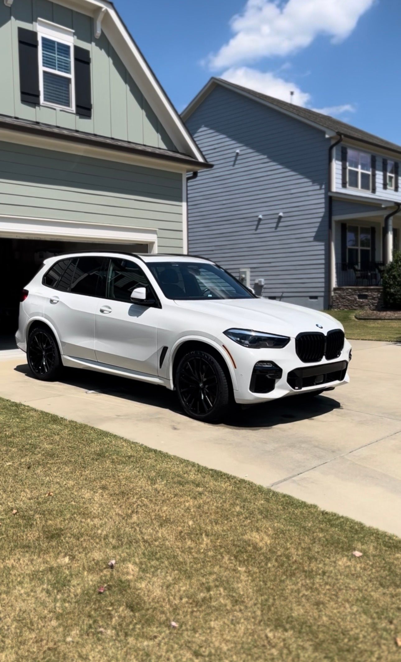 White BMW SUV parked in front of a house on a sunny day.