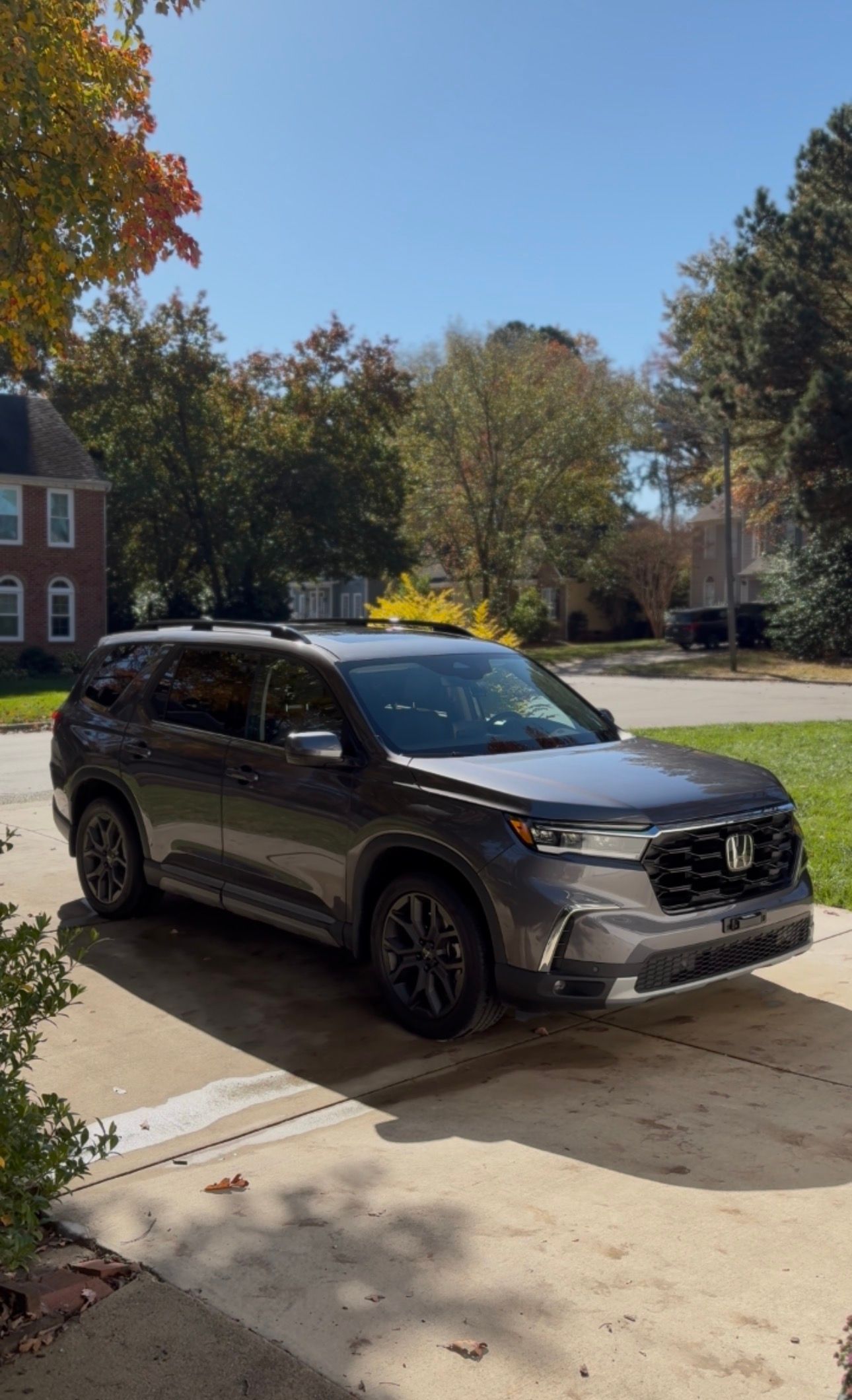 Dark gray Honda SUV parked on a paved driveway; sunny day with trees in the background.