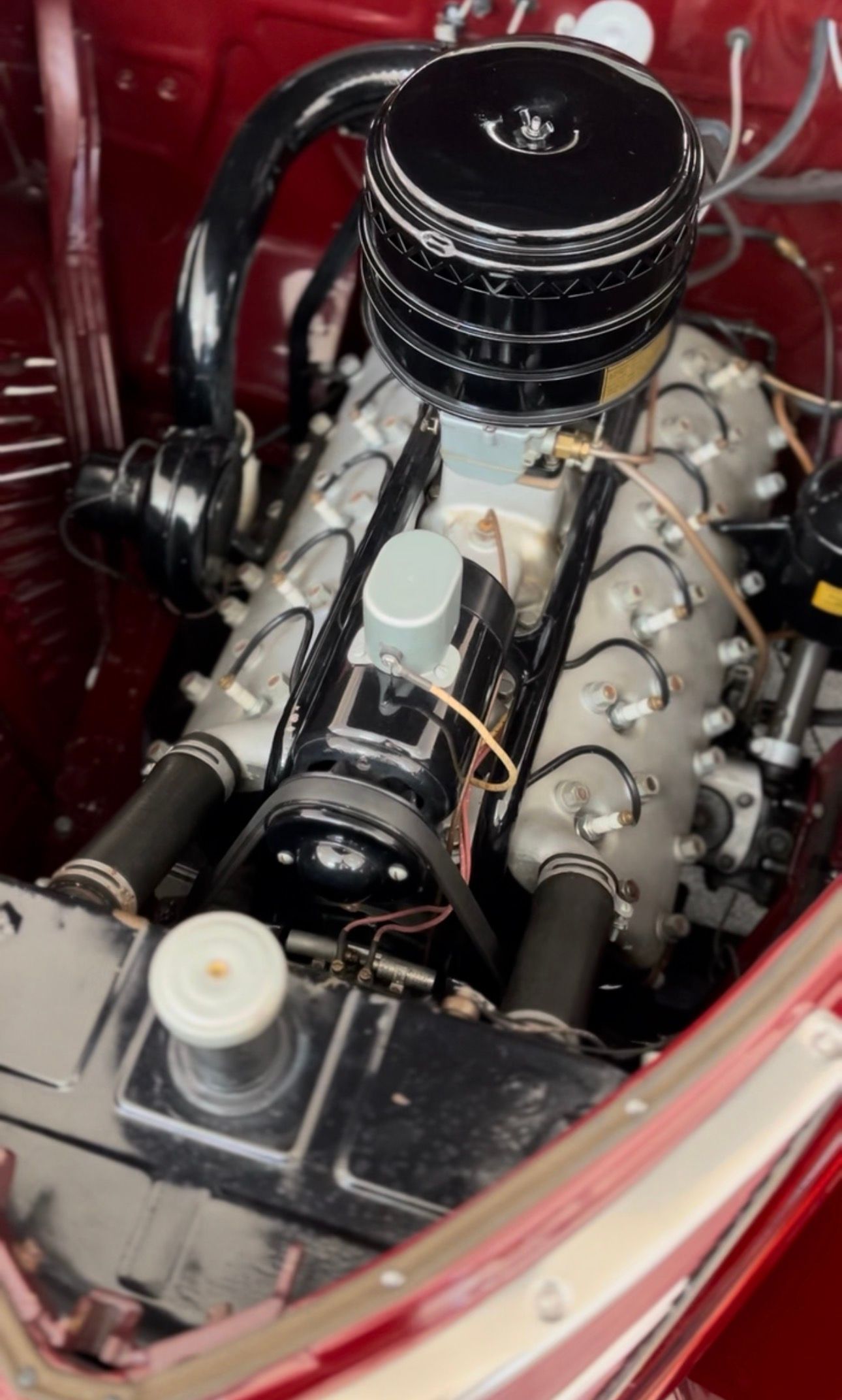 Close-up of a classic car engine; black and silver with a round air filter and radiator.