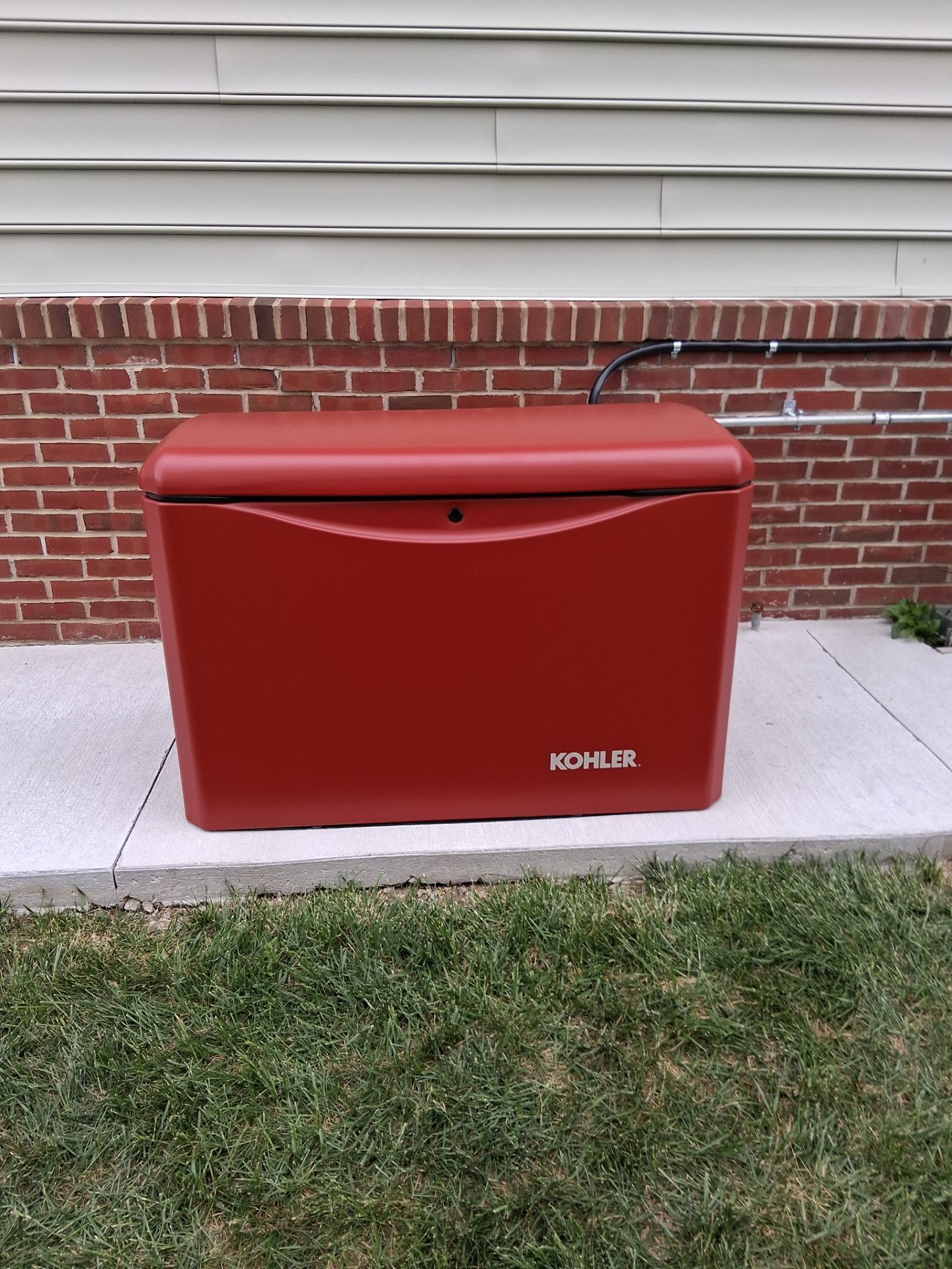 Red Kohler generator unit beside a brick house wall and window shutters.