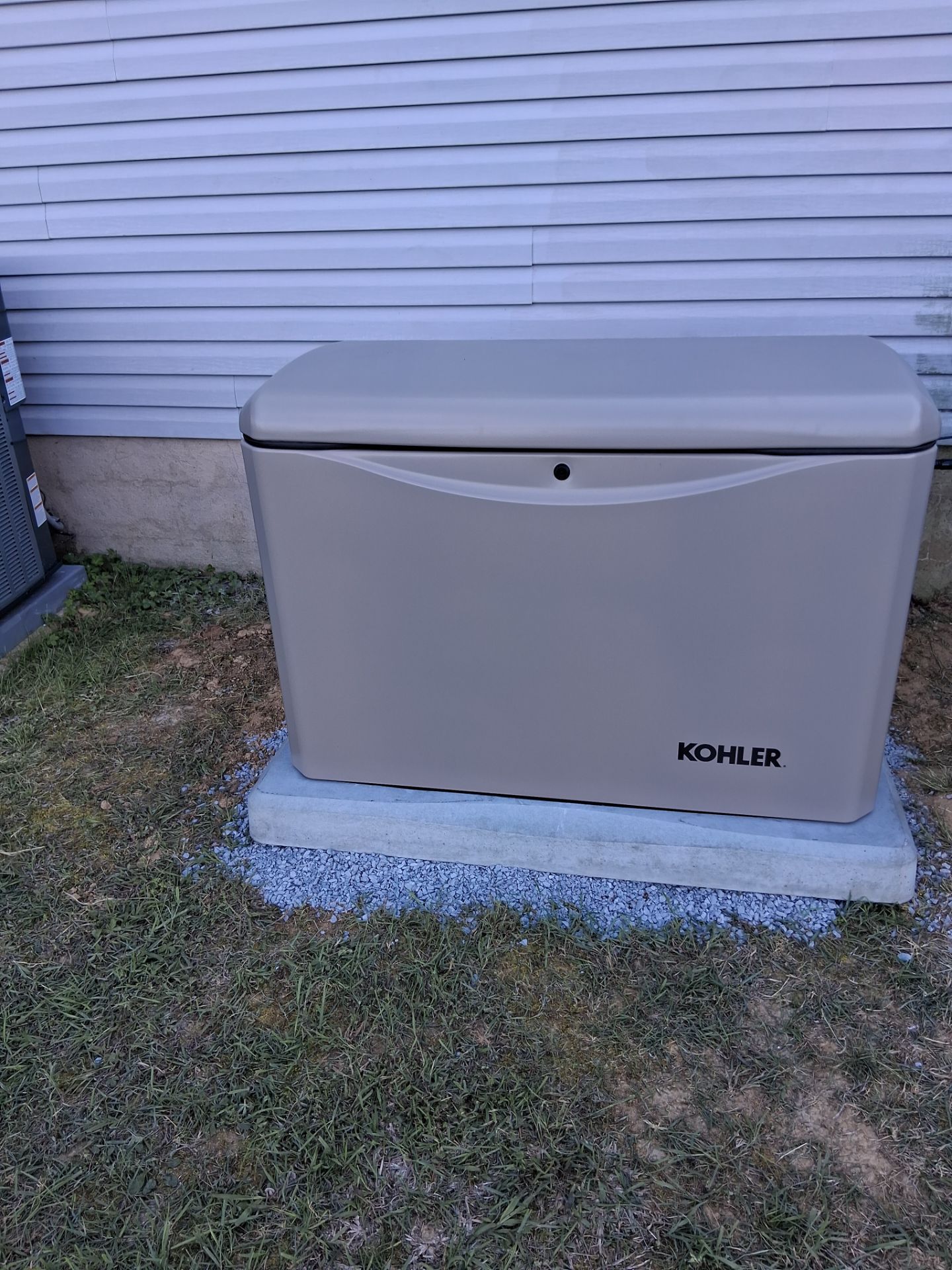 Gray outdoor storage box against a house wall on a concrete base, with a lawn in front.