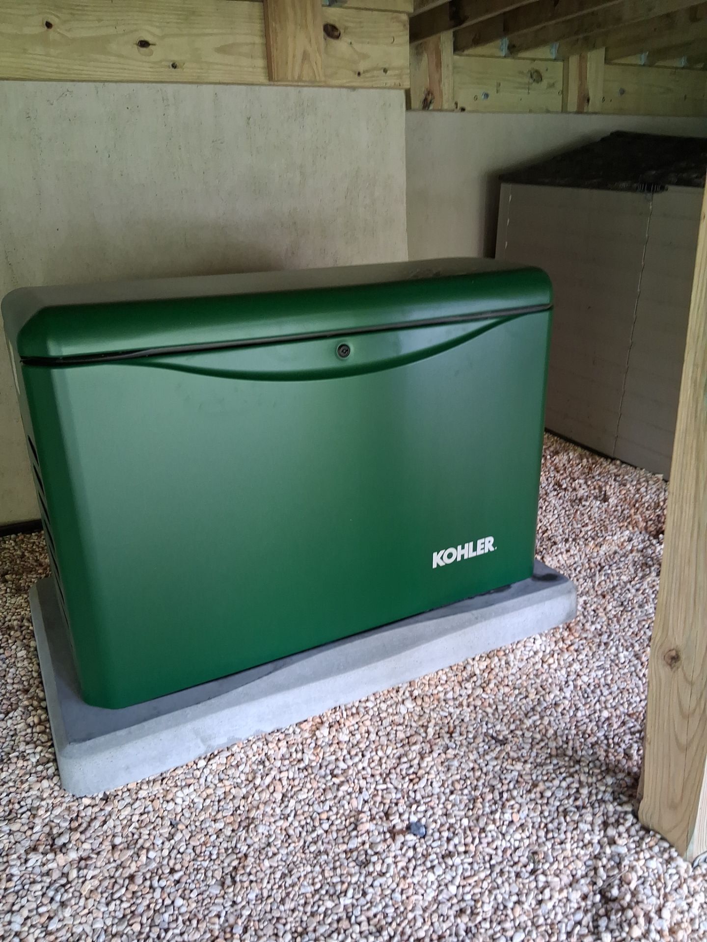 Green Kohler generator on a concrete pad under a covered outdoor structure.