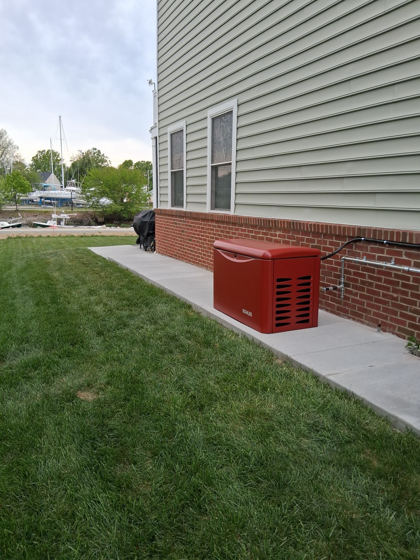 Red generator beside a house on a concrete walkway and grassy lawn