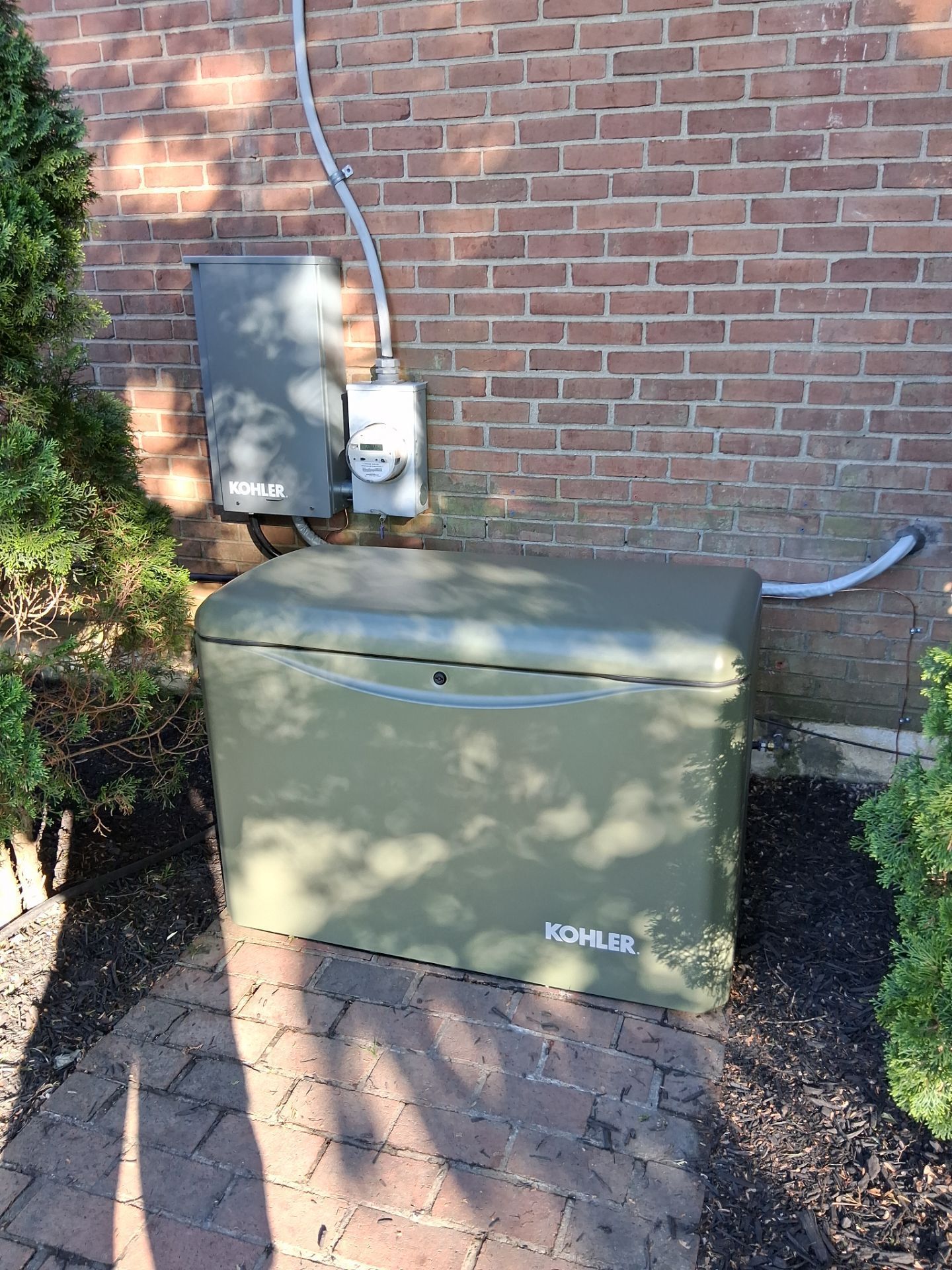 Green outdoor generator beside a brick wall with electrical conduit and meter box