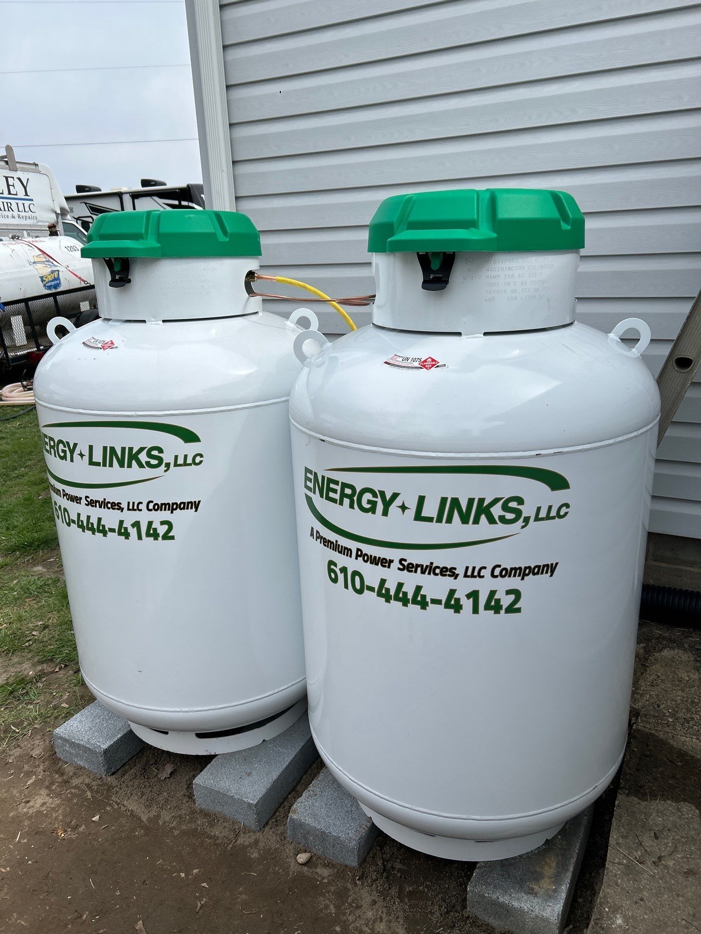 Two white ENERGY-LINKS propane tanks with green tops beside a building exterior.