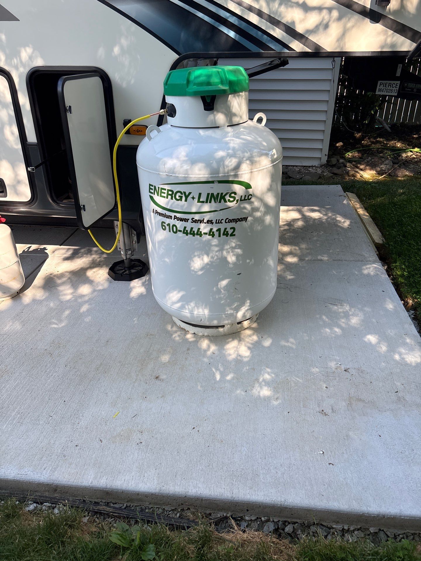 White propane tank with green cap on concrete beside a house and outdoor appliance.