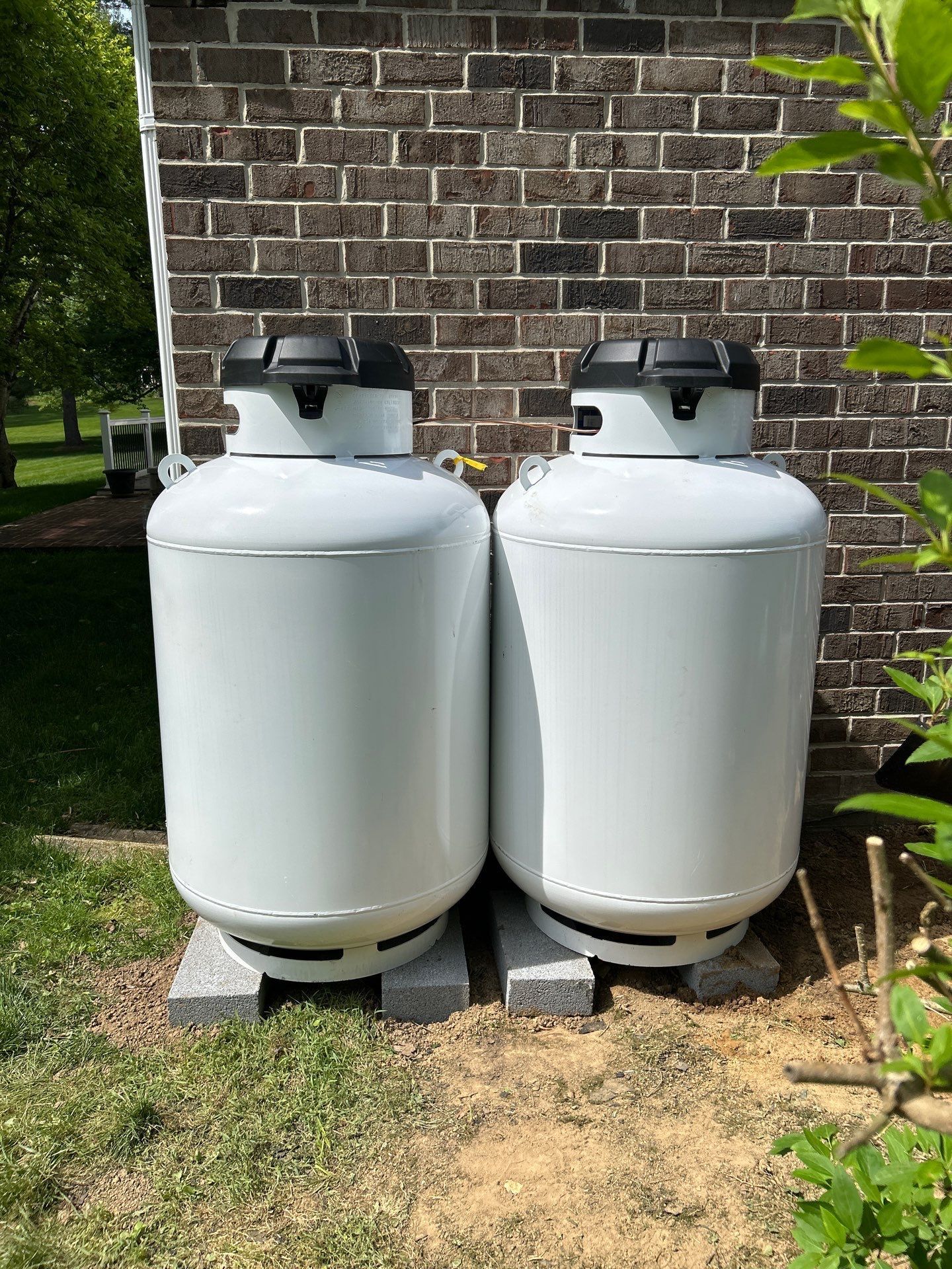 Two white propane tanks beside a brick wall on a grassy patio area