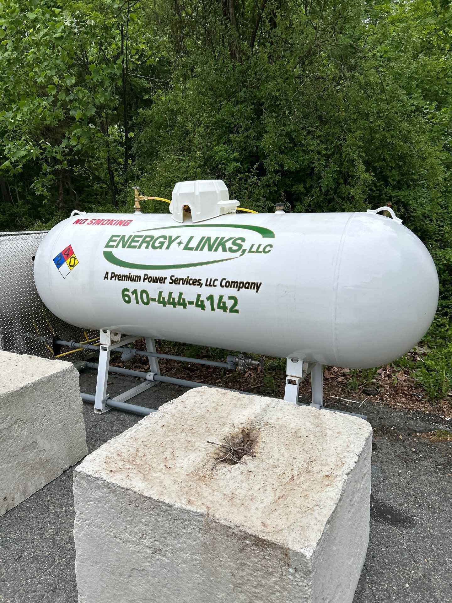 White propane tank labeled Energy-Livings LLC beside concrete blocks and trees