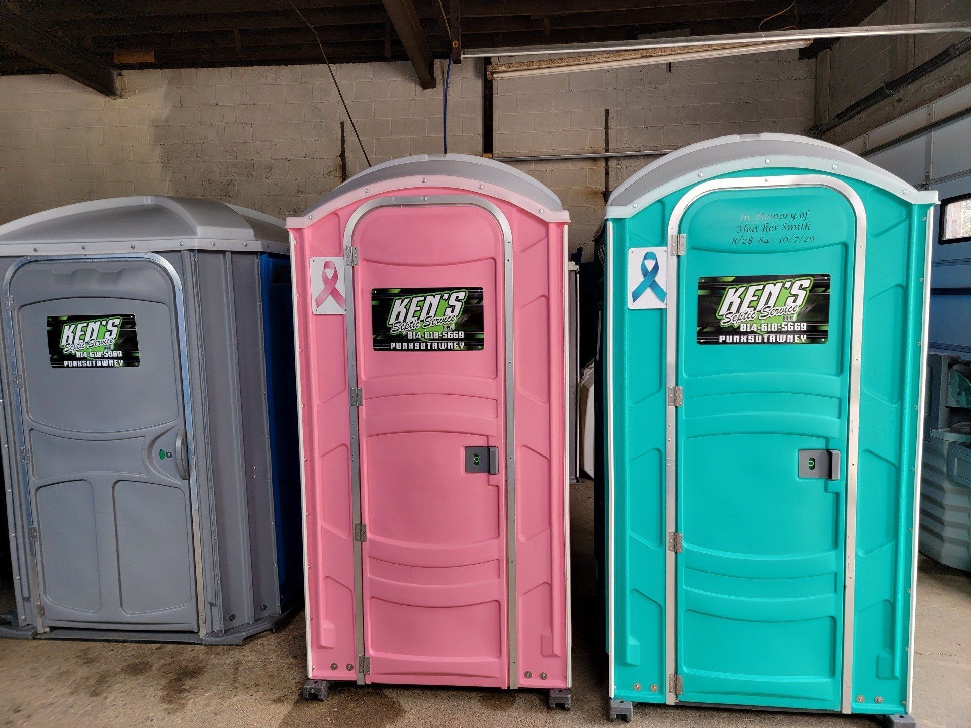 Three portable toilets are lined up in a warehouse.
