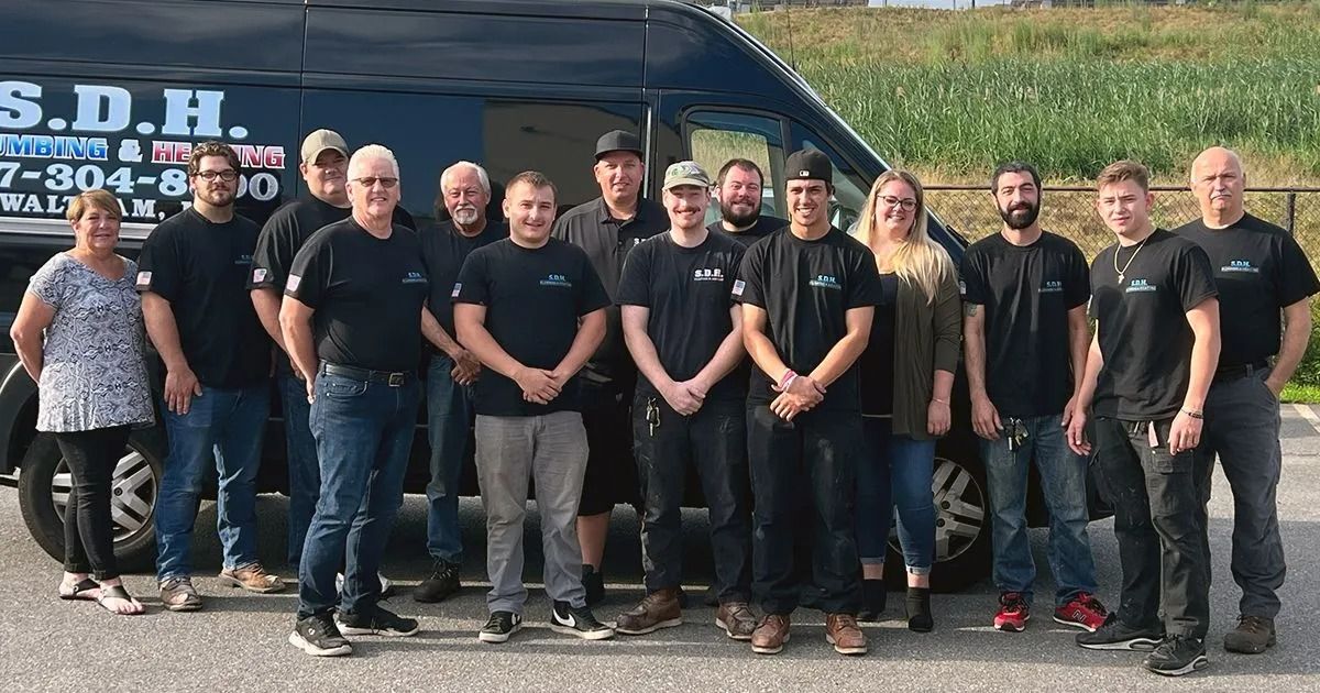 Group of people standing in front of a van; some wearing black t-shirts; outdoor setting.