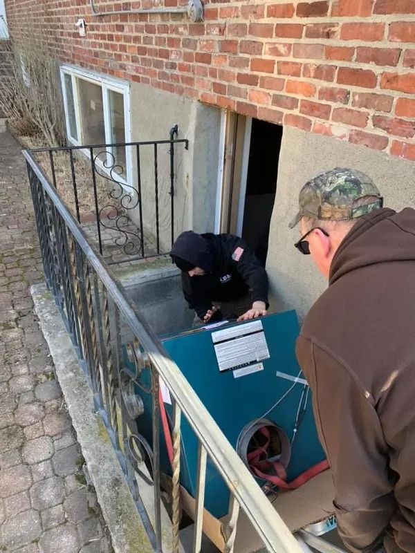 Two people move a teal box into a basement entrance with a wrought-iron railing.