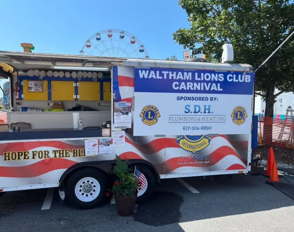 Waltham Lions Club Carnival food trailer with a Ferris wheel in the background. Sponsored by S.D.H. Plumbing & Heating.
