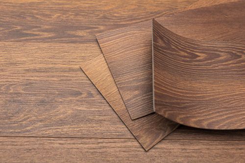 Brown wood-grain veneer sheets stacked on a matching wood surface, with one sheet curled at the corner