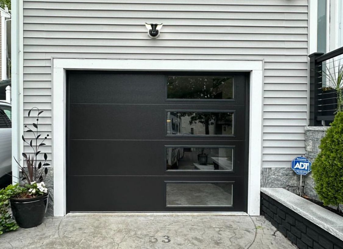 Modern black garage door with four window panels on a gray house exterior