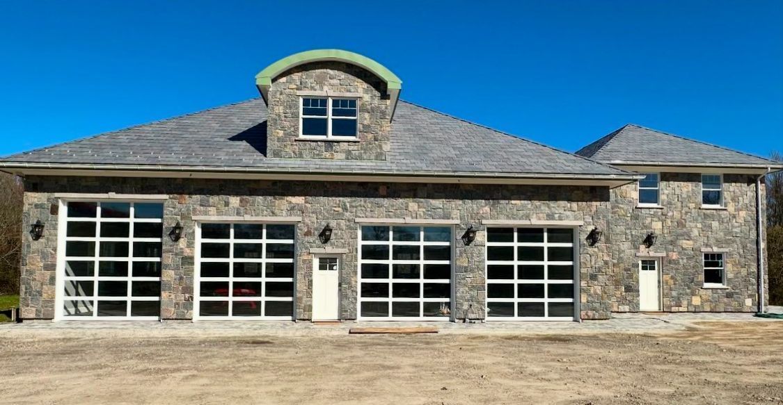 Stone house with multiple garage doors and a central arched dormer under a blue sky