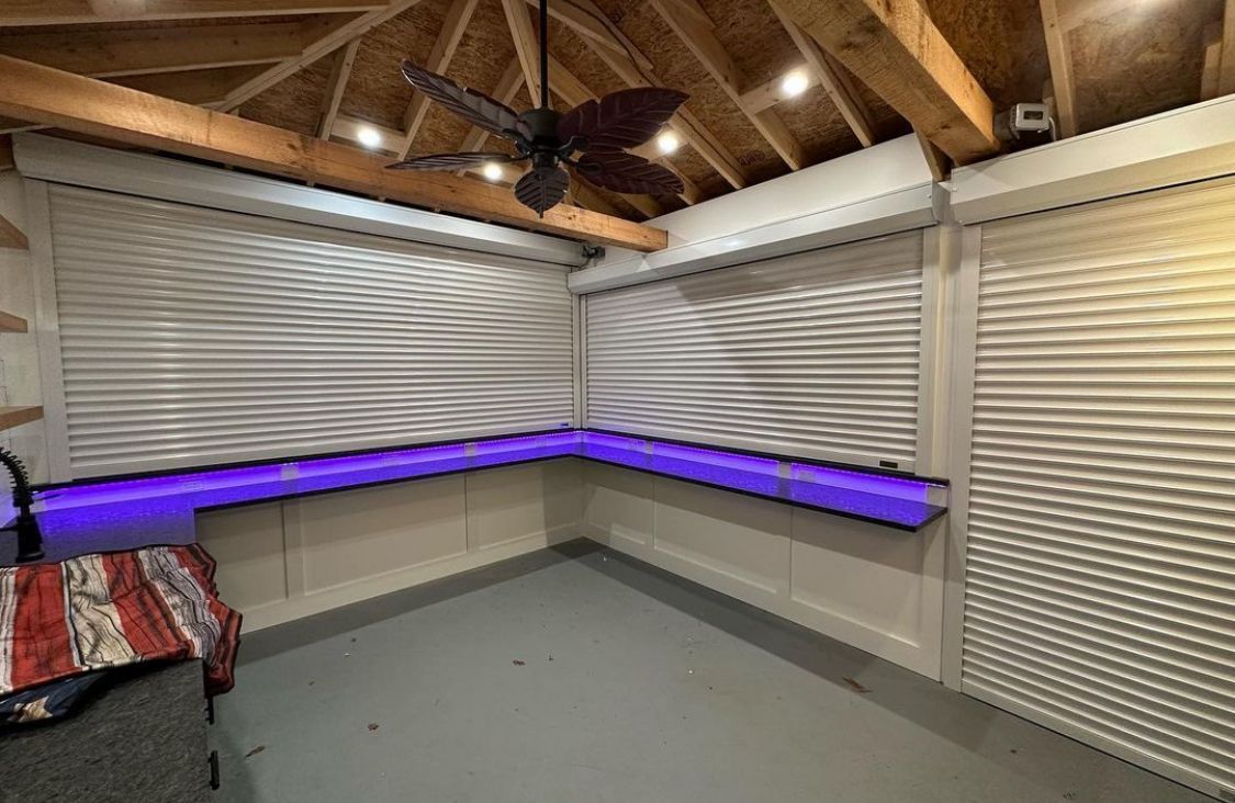 Small attic room with closed blinds, exposed wood beams, and purple LED strip lighting.