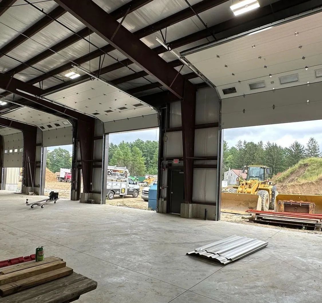 Inside a steel-frame building under construction, with concrete floor and heavy equipment visible outside open bays