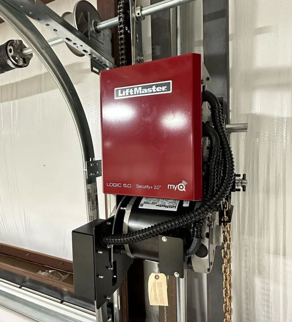 Red LiftMaster garage door opener mounted on a wall with hanging cables in a workshop setting