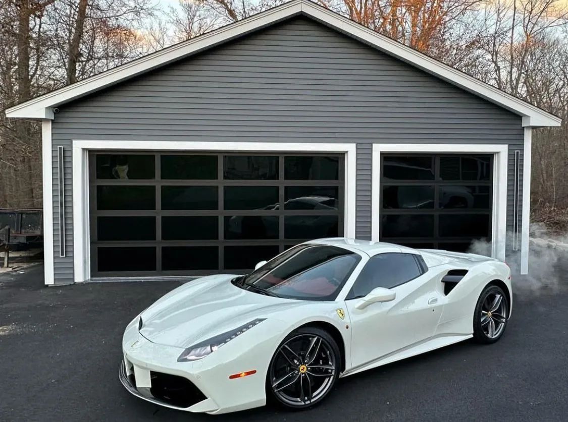 White sports car parked in front of a gray garage with two black doors