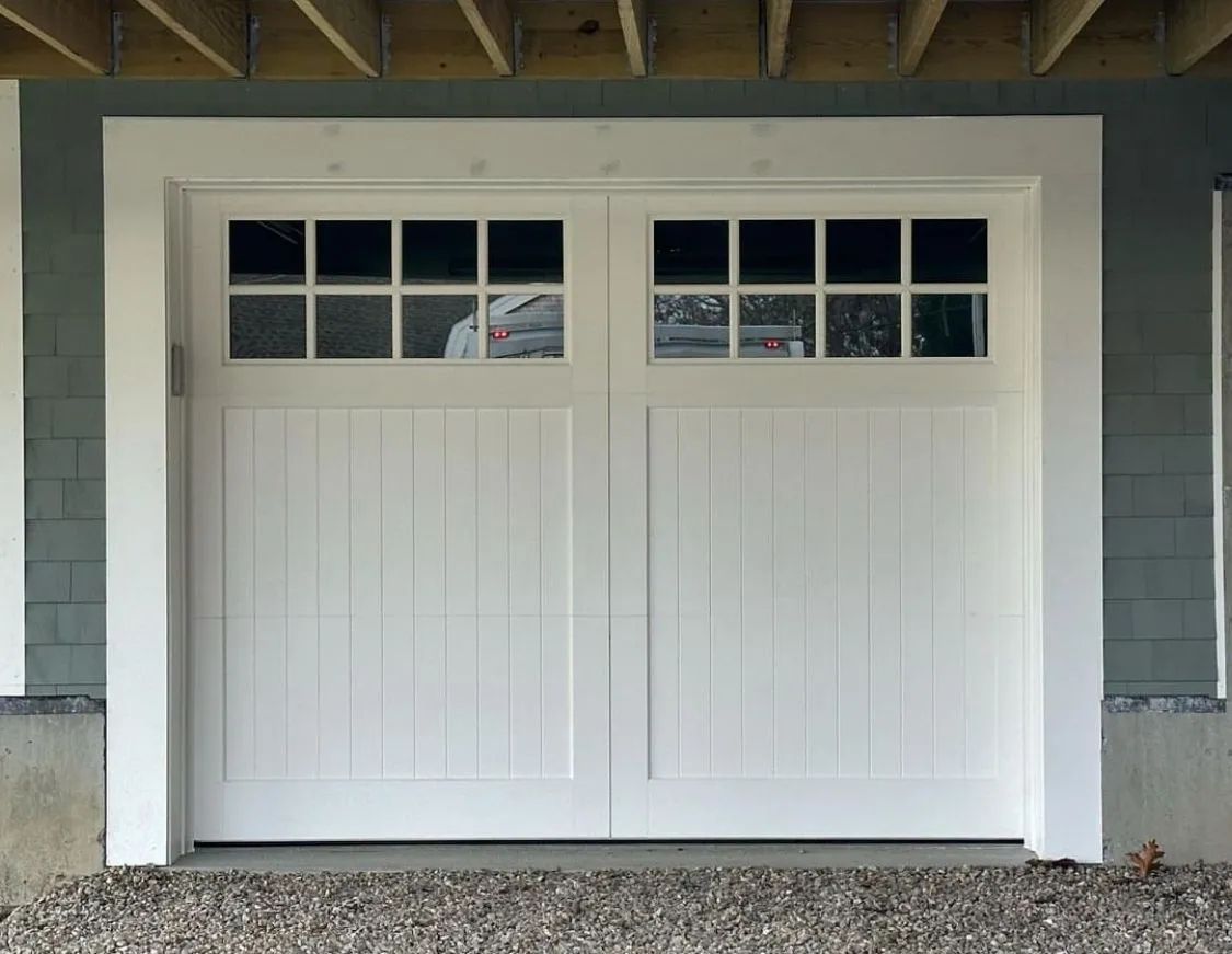 White double garage door with small windows under a gray exterior porch over gravel.